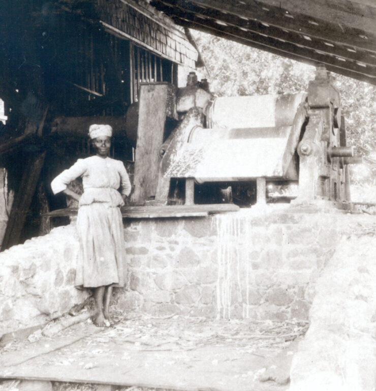 Black and white image of a black woman standing in front of a sugarcrushing machine