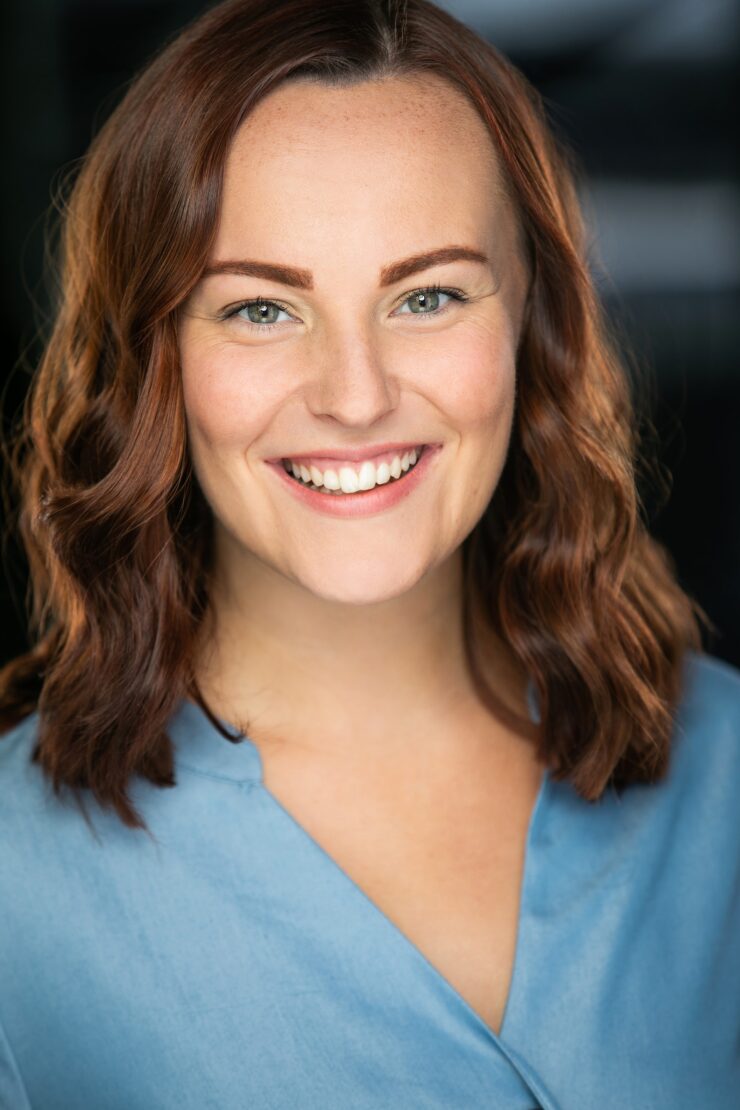 Headshot of young woman with long dark brown hair wearing a light blue top in front of a dark background.