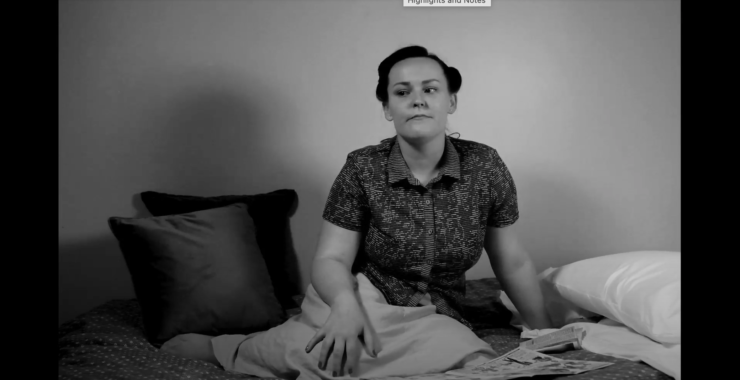 (Black and White) A young woman with a 1940s hairstyle sat on a bed with her feet tucked beneath her, surrounded by cushions.